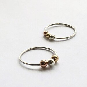 May include: Two silver rings with three beads each. The beads are silver, gold, and rose gold.