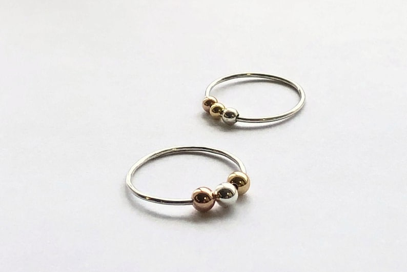 May include: Two silver rings with three beads each. The beads are silver, gold, and rose gold.