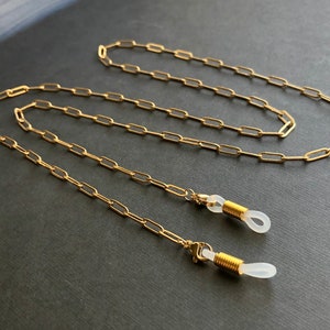 May include: Gold chain eyeglasses retainer with clear silicone ends. The chain is made of linked oval shapes.