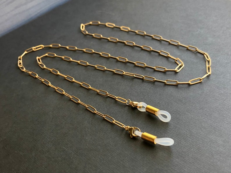 May include: Gold chain eyeglasses retainer with clear silicone ends. The chain is made of linked oval shapes.