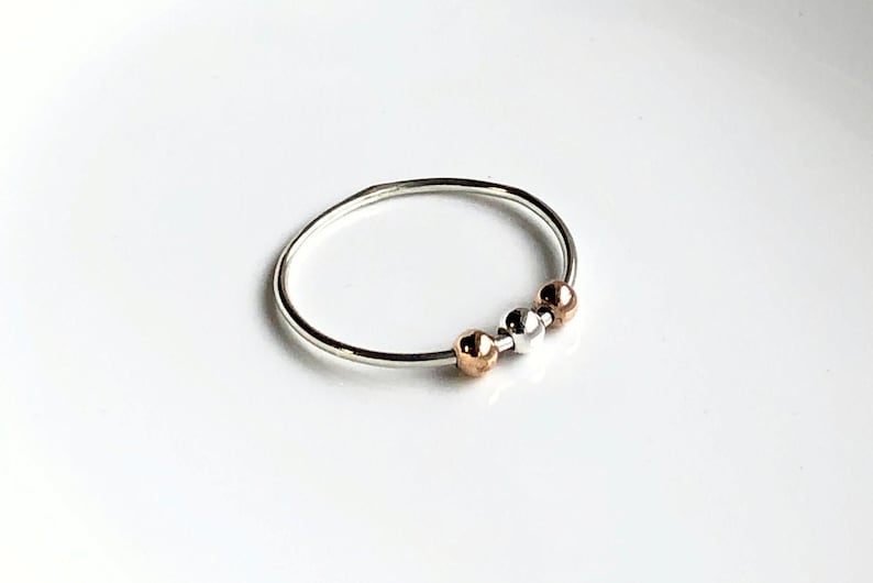 May include: A silver ring with three beads, one silver, one rose gold, and one gold.