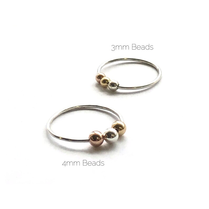 May include: Two silver hoop earrings with three beads each. The top hoop has 3mm beads and the bottom hoop has 4mm beads. The beads are silver, gold, and rose gold.
