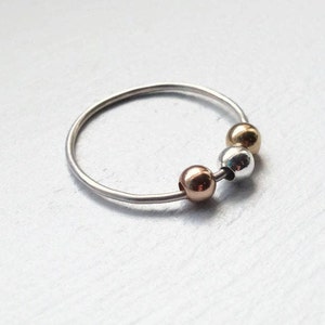 May include: A silver ring with three beads, one gold, one silver, and one rose gold.