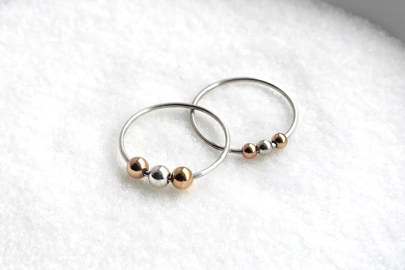 May include: Two silver rings with three beads each. The beads are silver, gold, and rose gold.