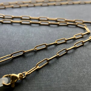 May include: A gold chain with a spring clasp. The chain is made of small, oval-shaped links.