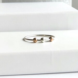 May include: A silver ring with three beads, one silver, one rose gold, and one silver.