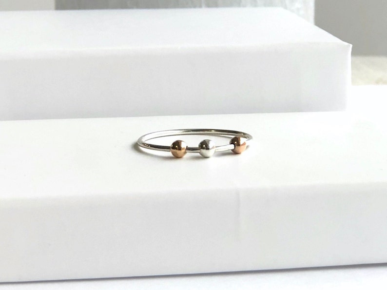 May include: A silver ring with three beads, one silver, one rose gold, and one silver.