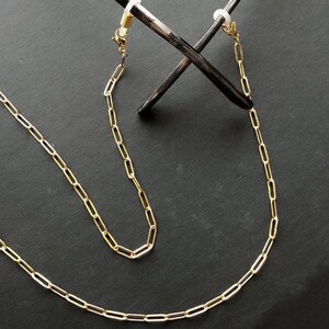 May include: A gold chain with two clasps, designed to hold glasses or sunglasses.