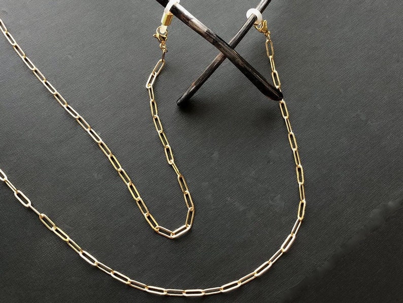 May include: A gold chain with two clasps, designed to hold glasses or sunglasses.