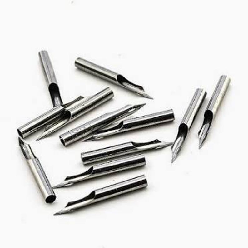 Puede incluir: Una colecci&oacute;n de plumillas de caligraf&iacute;a plateadas. Cada plumilla tiene una punta afilada y una ranura central. Las plumillas son cil&iacute;ndricas con un agujero para la tinta.