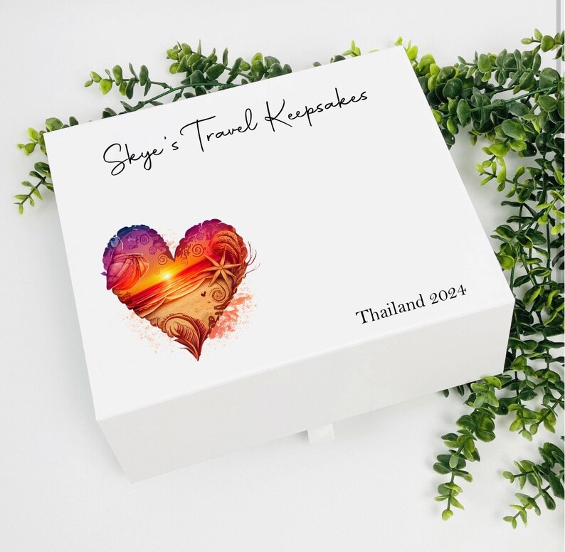 May include: White keepsake box with a heart-shaped design featuring a sunset over the ocean. The box is labeled "Skye's Travel Keepsakes" and "Thailand 2024".