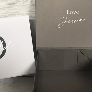 Pu&ograve; includere: Una scatola regalo bianca con una lettera nera "D" e la parola "Daddy" scritta in corsivo. Il coperchio della scatola &egrave; grigio e ha le parole "Love Jessica" scritte in corsivo bianco.