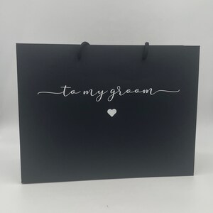 Puede incluir: Bolsa de regalo negra con texto blanco que dice "a mi novio" y un peque&ntilde;o coraz&oacute;n blanco.