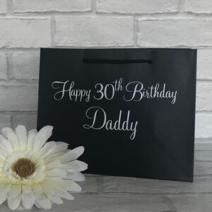 May include: Black gift bag with white text that reads "Happy 30th Birthday Daddy".