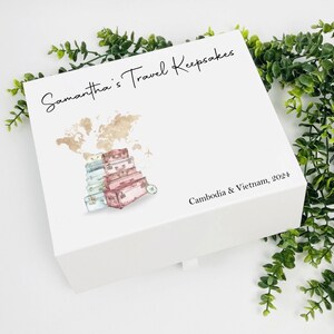May include: White keepsake box with a world map and stacked suitcases illustration. The text "Samantha's Travel Keepsakes" is on the top and "Cambodia & Vietnam, 2024" is on the bottom.