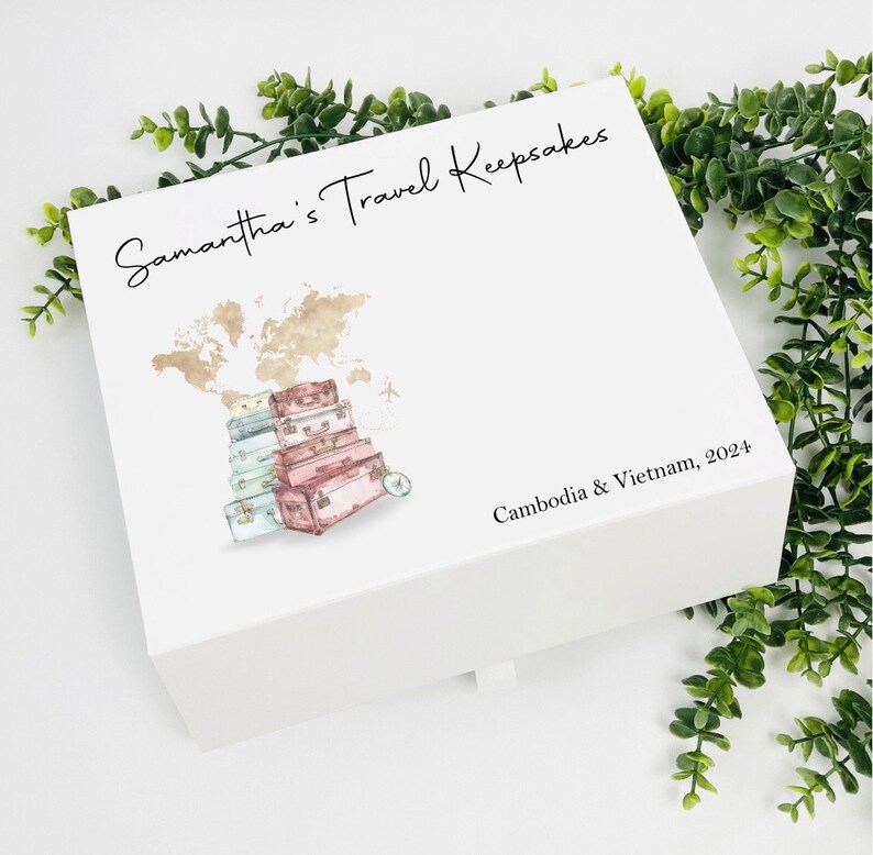 May include: White keepsake box with a world map and stacked suitcases illustration. The text "Samantha's Travel Keepsakes" is on the top and "Cambodia & Vietnam, 2024" is on the bottom.