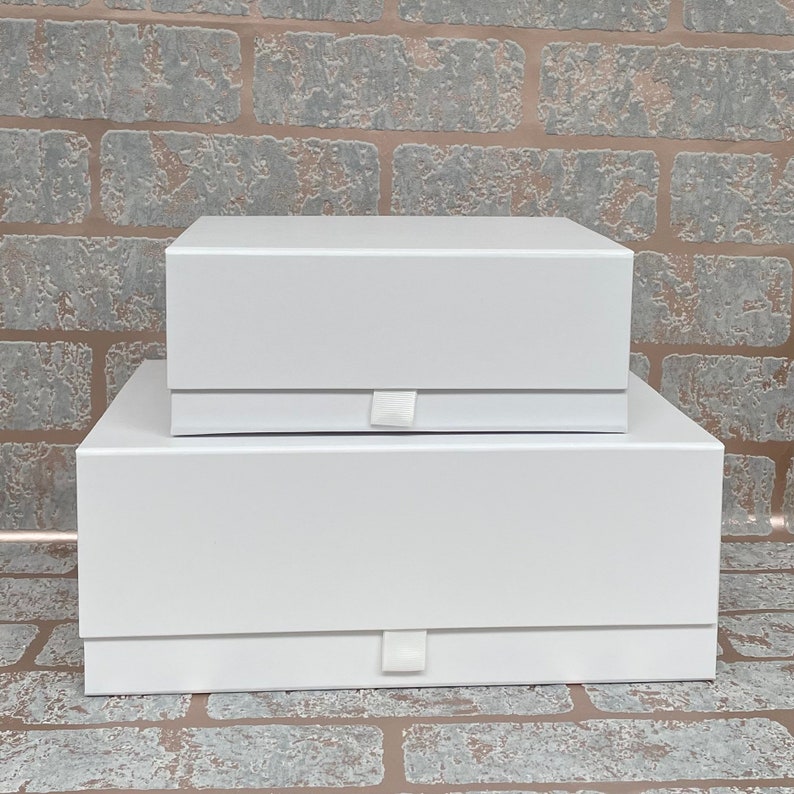 May include: Two white gift boxes stacked on top of each other. The boxes have a simple design with a white ribbon closure.