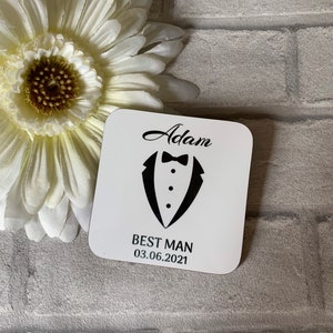 May include: White square coaster with black text and a tuxedo graphic. The text reads "Adam Best Man 03.06.2021".