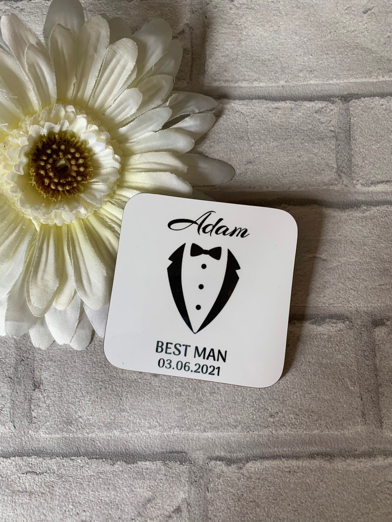 May include: White square coaster with black text and a tuxedo graphic. The text reads "Adam Best Man 03.06.2021".