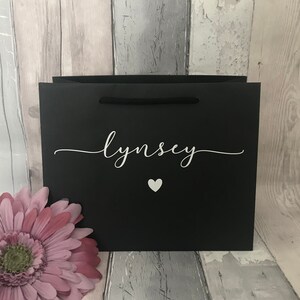 May include: Black gift bag with a white heart and the name "Lynsey" printed on it.