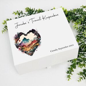 May include: White keepsake box with a heart-shaped design featuring a watercolor landscape of mountains and a winding road. The text "Jacob's Travel Keepsakes" and "Canada, September 2024" is printed on the box.