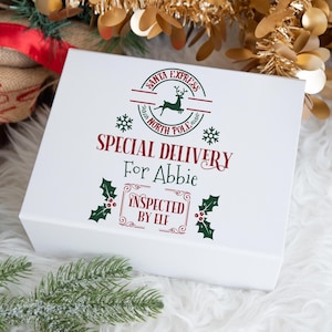 May include: A white gift box featuring festive text and graphics. The box reads "Santa Express North Pole" and "Special Delivery For Abbie" in red and green. Decorated with snowflakes, holly, and a reindeer, it has a Christmas theme.