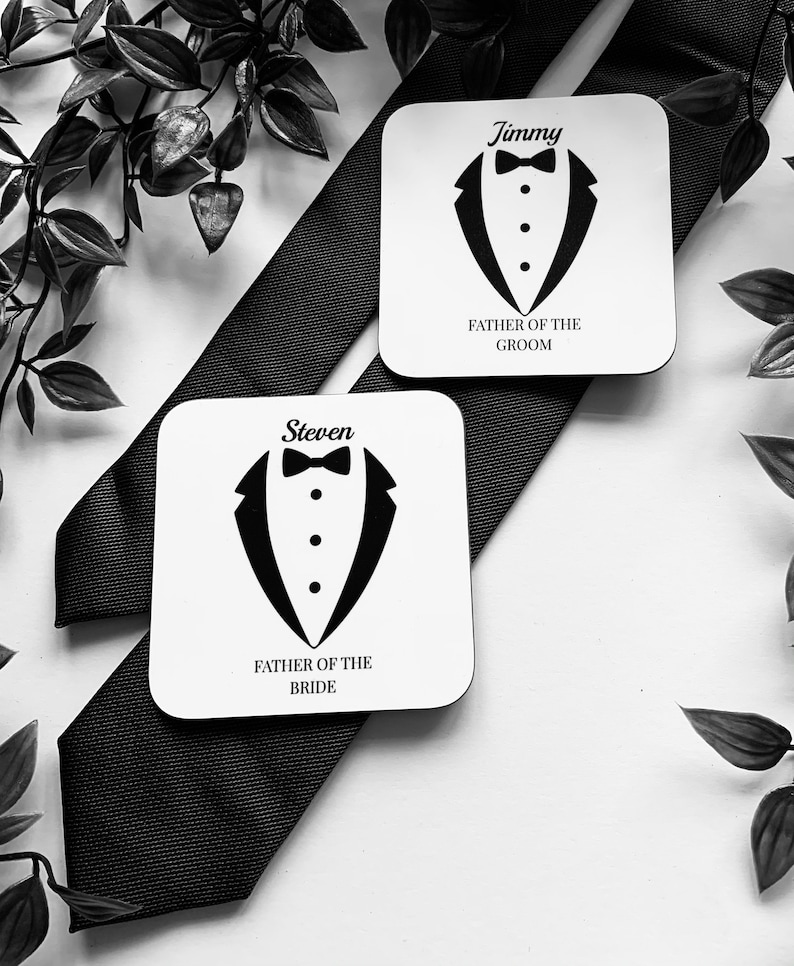 May include: Two white square coasters with black tuxedo designs and the text "Father of the Groom" and "Father of the Bride". The coasters have the names "Jimmy" and "Steven" printed on them.