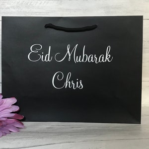 May include: Black gift bag with white text that reads "Eid Mubarak Chris".