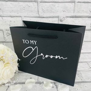 May include: Black gift bag with white text that says "To My Groom".