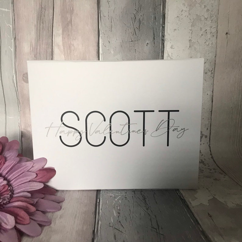 May include: White card with black text that reads "SCOTT" and "Happy Valentine's Day" in cursive.