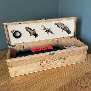 May include: A wooden box containing a bottle of red wine, a corkscrew, a bottle stopper, and a wine pourer. The box is engraved with the message "Merry Christmas Love from Jacob & Paige".