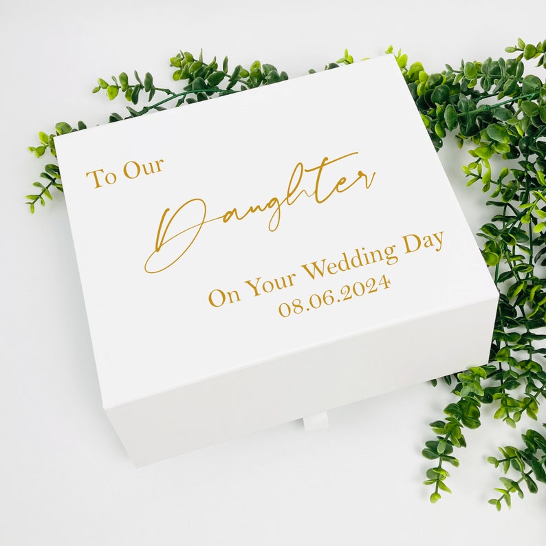 May include: White gift box with a gold inscription that reads "To Our Daughter On Your Wedding Day 08.06.2024".