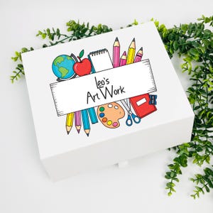 May include: A white art box featuring a colourful illustration of art supplies, including pencils, a globe, an apple, and a palette. The box has the text "Leo's Art Work" on the front.