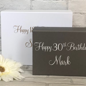 May include: Two gift boxes, one white and one gray. The white box has the text "Happy 18th" in brown lettering. The gray box has the text "Happy 30th Birthday Mark" in white lettering.