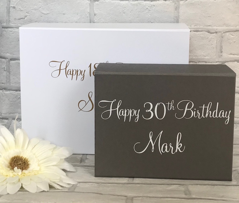 May include: Two gift boxes, one white and one gray. The white box has the text "Happy 18th" in brown lettering. The gray box has the text "Happy 30th Birthday Mark" in white lettering.
