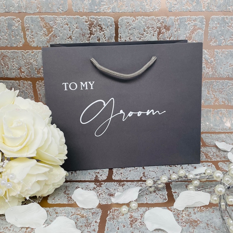 May include: A gray gift bag with a white rope handle. The bag has the text "To My Groom" printed on the front in white.