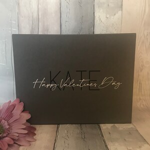 May include: A dark gray gift box with the text "KATE Happy Valentines Day" in black and white lettering.