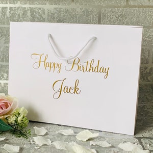 May include: White gift bag with a gold inscription that reads "Happy Birthday Jack".
