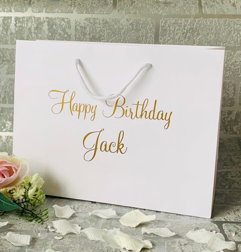 May include: White gift bag with a gold inscription that reads "Happy Birthday Jack".