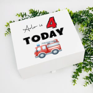 Könnte beinhalten: Weiße Geschenkbox mit einer roten Feuerwehrwagen-Illustration und dem Text "Arlo is 4 TODAY" in schwarzen Buchstaben.