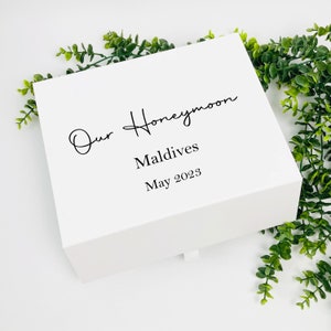 Può includere: Scatola regalo bianca con il testo "Our Honeymoon Maldives May 2023" scritto in corsivo nero.