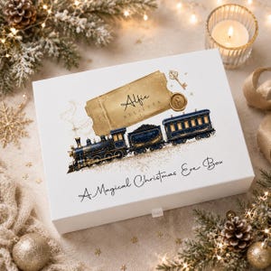 Peut inclure: Une boîte rectangulaire blanche pour le réveillon de Noël avec un graphique de billet doré portant le texte Alfie Believes, une illustration de train à vapeur bleu foncé et le texte A Magical Christmas Eve Box écrit en noir sur le devant.