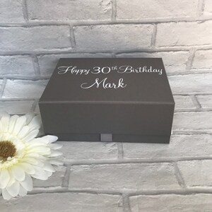 May include: A gray gift box with a white ribbon and the text "Happy 30th Birthday Mark" on the top.