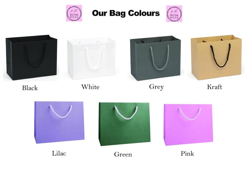 May include: Our Bag Colours: A selection of paper gift bags in various colors, including black, white, grey, kraft, lilac, green, and pink. Each bag has a white rope handle.