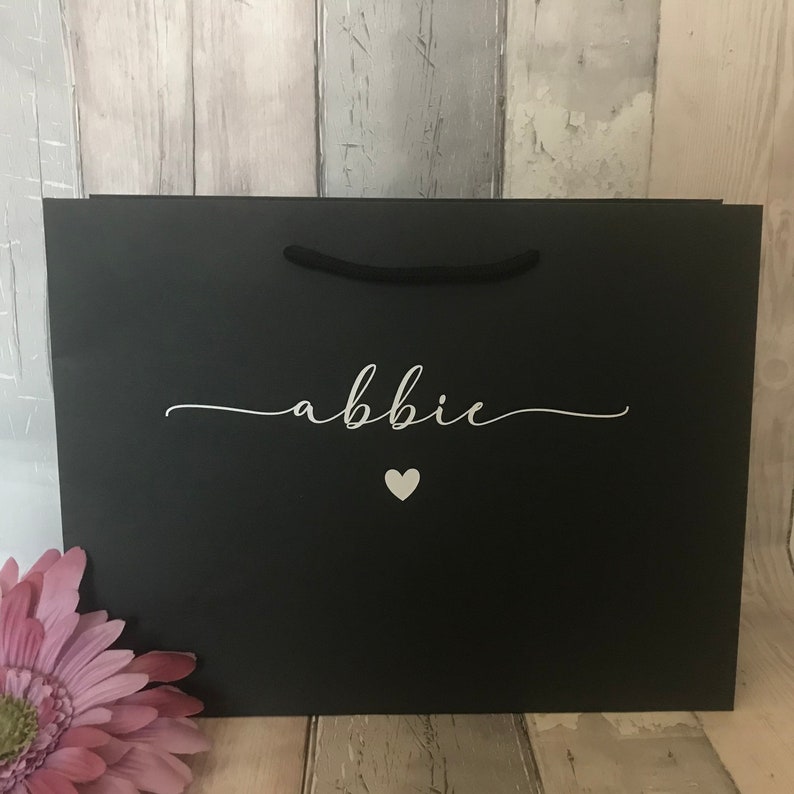 May include: A black gift bag with a white heart and the name "abbie" written in cursive.