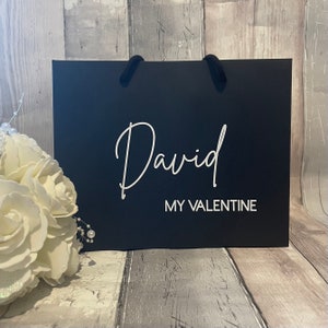 Może przedstawiać: Czarna torba prezentowa z białym tekstem, kt&oacute;ry brzmi "David My Valentine".
