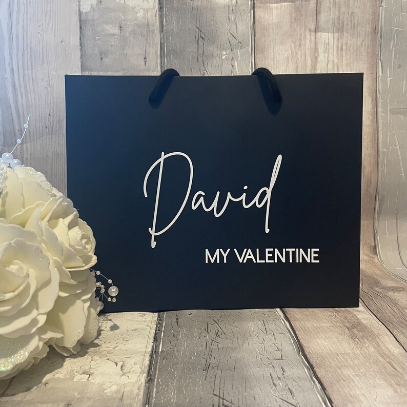 Może przedstawiać: Czarna torba prezentowa z białym tekstem, kt&oacute;ry brzmi "David My Valentine".