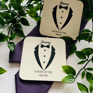 May include: Two white square coasters with black tuxedo designs and text. The top coaster says "Steven Father of the Bride". The bottom coaster says "Jimmy Father of the Groom".