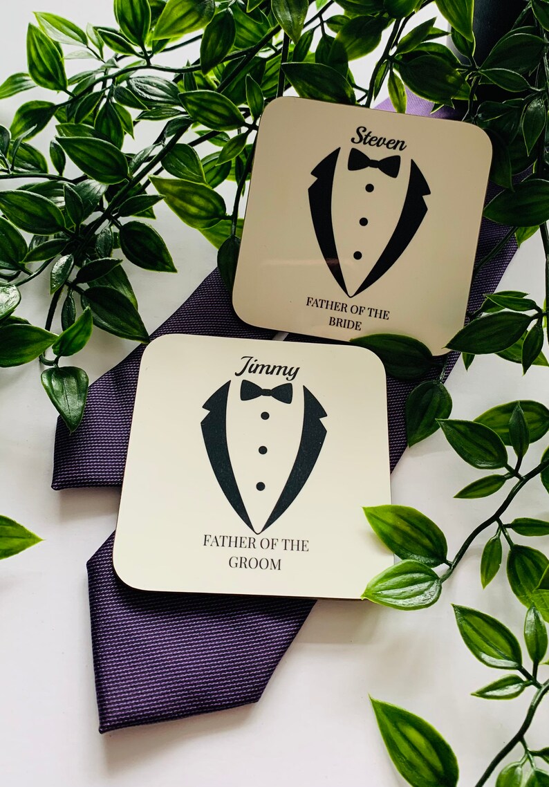 May include: Two white square coasters with black tuxedo designs and text. The top coaster says "Steven Father of the Bride". The bottom coaster says "Jimmy Father of the Groom".
