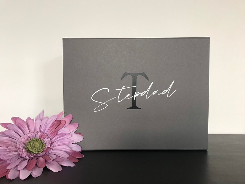 Pu&ograve; includere: Una scatola regalo grigia con una lettera "T" bianca e la parola "Stepdad" scritta in corsivo.